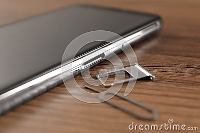 SIM card tray, mobile phone and ejector tool on wooden table, closeup Stock Photo