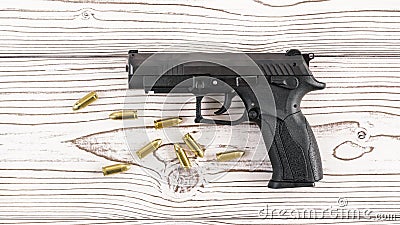 Simple black modern pistol gun with few yellow brass bullets on white wooden board, view from above Stock Photo