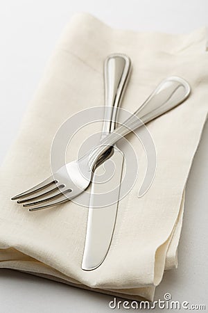 Simple, casual fine dining place setting with high quality silverware fork and knife on white linen napkin with white tablecloth Stock Photo