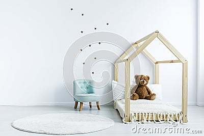 Simple kid room interior with diy bed with a teddy bear, armchair, round rug and stars on the wall. Place for your product Stock Photo