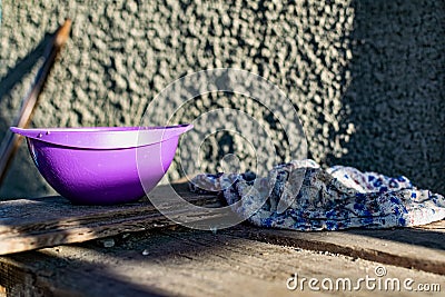 A simple purple plastic plate, outdoor tableware for feeding animals, cats and dogs, stands on dusty wooden planks Stock Photo