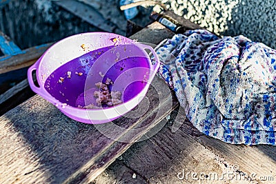 A simple purple plastic plate, outdoor tableware for feeding animals, cats and dogs, stands on dusty wooden planks Stock Photo