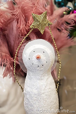 Simple sparkly Christmas snowman decoration holding glitter gold star over its head in front of pink feathers and baubles Stock Photo