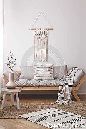 Simple, wooden stool on a wicker rug in a peaceful living room interior with a beautiful handmade decoration on a white wall Stock Photo