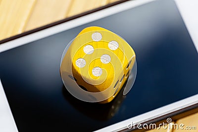 Simple yellow game dice showing six laying on a modern smartphone screen. Dice with 6 on it placed on a mobile phone display Stock Photo