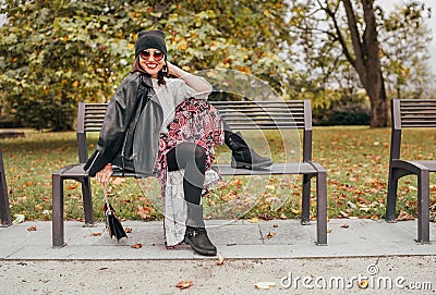 Sincerely laughing female dressed fashion boho style colorful long dress, warm knitted sweater with black leather biker jacket and Stock Photo