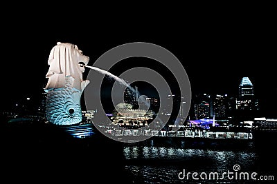 Singapore:August 20, 2023- Side view of Merlion spraying the water with cityscape at night and lake in background Editorial Stock Photo