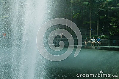 People with face masks relaxing at Rain Vortex fountain at Changi Airport Jewel. High speed capture of water Editorial Stock Photo