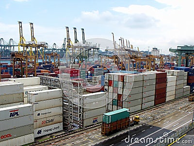 Transport truck moves two containers in the storage area. Dozens of stacked containers and large cranes in the background at the S Editorial Stock Photo