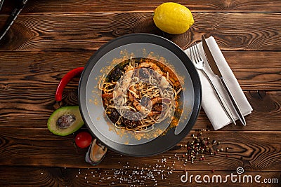 Singapore-style noodles with mushrooms and shrimps in a black plate on a wooden background Stock Photo