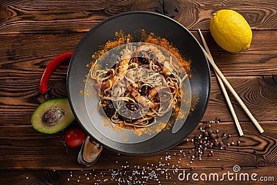 Singapore-style noodles with shiitake mushrooms and shrimps in a black plate on a wooden background Stock Photo