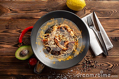 Singapore-style noodles with shiitake mushrooms and shrimps in a black plate on a wooden background Stock Photo