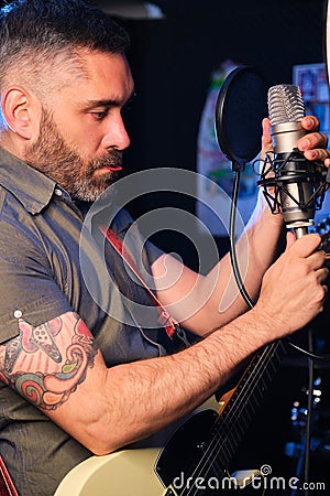 Singer and guitarist adjusting the microphone before recording at studio. Stock Photo