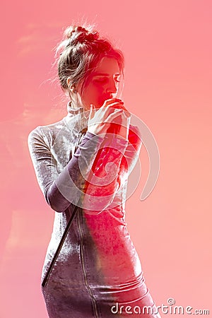 Singing Caucasian Lady In Gray Reflective Dress Posing With Radio Microphone Over Pink Background with Added Lightflares Stock Photo