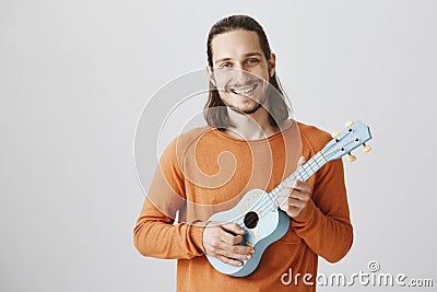 Singing song during travel in train. Portrait of friendly handsome male in orange sweater holding ukulele, playing Stock Photo