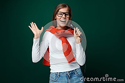 Singing young woman holding microphone on green background Stock Photo