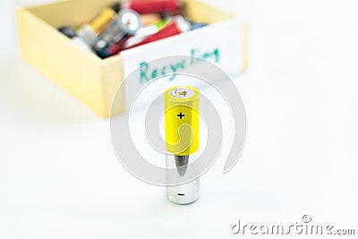 A single AA battery in front of a box with used batteries with the word recycling ready for the correct disposal of substances Stock Photo