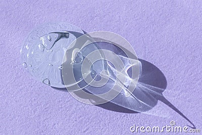 Single blob of transparent glycerin or gel smear smudge swatch on lilac backdrop with shadow. Glossy texture with tiny Stock Photo