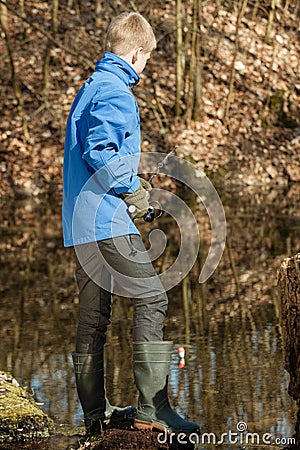 Single boy in blue jacket at pond fishing alone Stock Photo