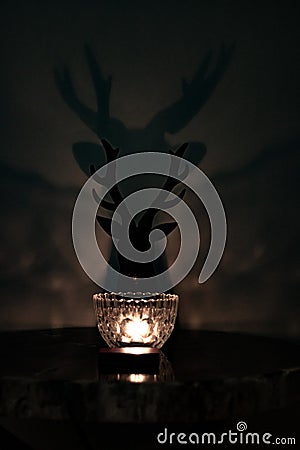 Single candle glowing with silhouette of deer head with antlers outlined against the wall Stock Photo