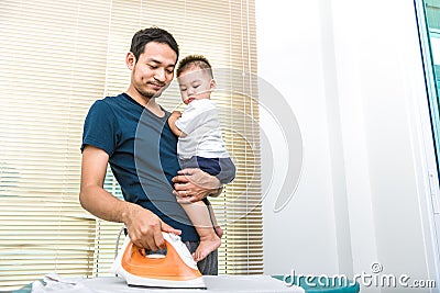 Single dad is ironing while carrying his son. People and Lifestyles concept. Stock Photo