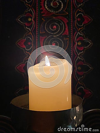 A single glowing pillar candle backed by Chinese handiwork Stock Photo