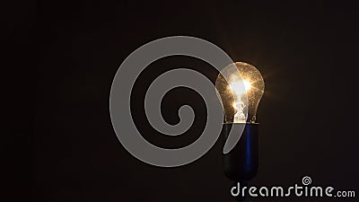 Single illuminated light bulb isolated on black background. Close-up of a glowing incandescent tungsten lamp yellow orange color Stock Photo