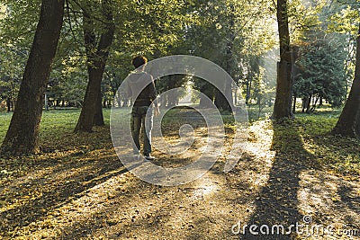 Single man person back to camera stay in park outdoor space on a lonely trail road autumn season time morning sun rays Stock Photo