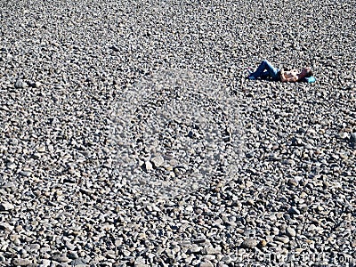 A single man sleeping in the sun on a grey pebble beach in Funchal, Madeira Editorial Stock Photo