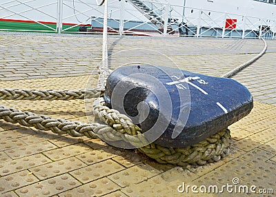 A single mooring device with coiled ropes keeps the ship on the dock. Stock Photo