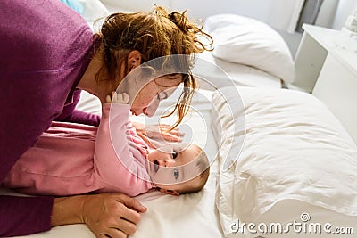 Single mother waking up her baby lying on the bed making gestures of laughter and happiness Stock Photo