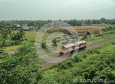 Single orange diesel engine locomotive drives on the railway pass through the rice field Editorial Stock Photo