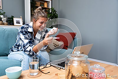 Single sad woman complaining holding a pregnancy test sitting on a couch in the living room at home, Stressed female, Positive or Stock Photo