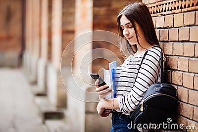 Single student walking and reading mobile phone messages with a university building in the background Stock Photo