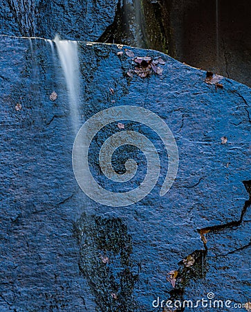 Single, tiny waterfall against shaded blue rock Stock Photo