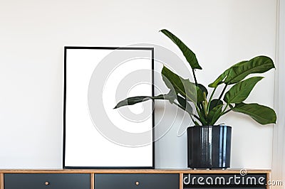 Single vertical black fram with white mockup area next to green potted plant on Scandinavian design sideboard against white wall Stock Photo