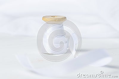 Single Wooden Spool Roll with Silk Ribbon on White Cotton Linen Fabric Background. Sewing Crafts Hobby Concept. Stock Photo