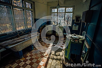 Creepy old laundry room with a dirty floor and broken wash machines and bathes in an abandoned psychiatric hospital. Stock Photo