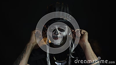 Sinister man with horrible Halloween skeleton makeup puts on headphones, starts dancing, celebrating Stock Photo