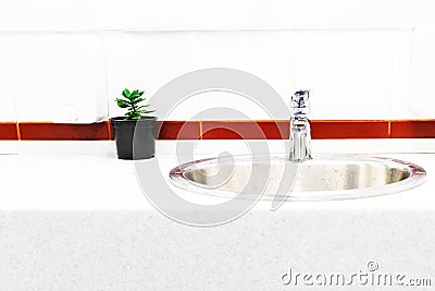 The sink in the bathroom on the background of bright tiles with a bright stripe, the design of a flower in a pot Stock Photo