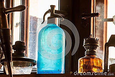 Siphon for soda water. A vintage blue glass soda siphon stands on a shelf surrounded by ancient artifacts. Stock Photo