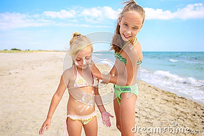 Sister applying protective sunscreen on child. Girl draws sun cream on her stomach Stock Photo