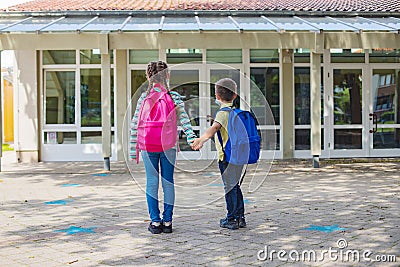 Sister and brother return to school after vacation. Children hold hands in front of school doors. The new school year Stock Photo