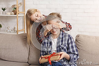 Sister Covering Brother`s Eyes Giving Birthday Gift Sitting At Home Stock Photo