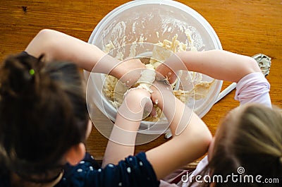 Sisters preparing dough for bread or cake with their hands in a plastic bowl Stock Photo