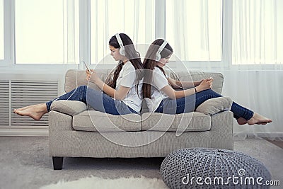 Sisters teenage girls with smart phone and headphones listening music and ommunicate in social networks Stock Photo