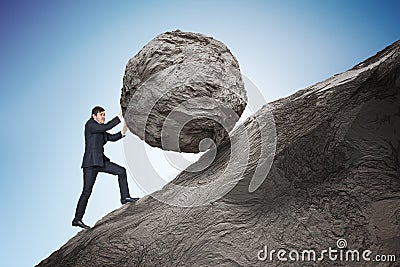 Sisyphus metaphore. Young businessman pushing heavy stone boulder up on hill Stock Photo