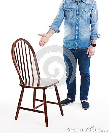 Sit down please. A man in casual style wear shows wooden rustic chair. Man and chair isolated on white background. Stock Photo