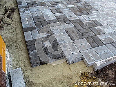 Site with unfinished work on laying gray Brick paving slabs. Sandy base, curb and sidewalk blocks. Construction background with Stock Photo