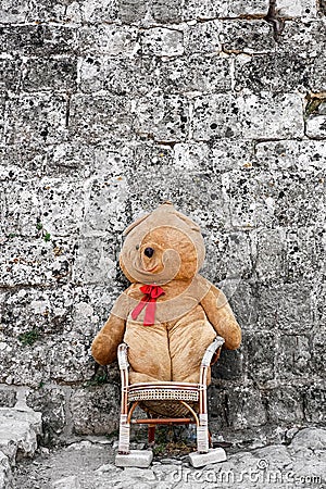 Sitting big teddy bear on a chair outside building Stock Photo